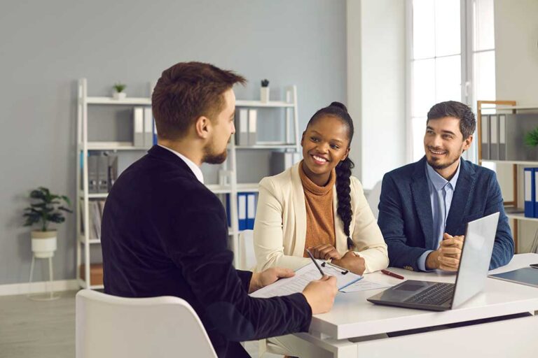 A family stands with a real estate agent, reviewing documents in a bright, lived-in living room surrounded by moving boxes.